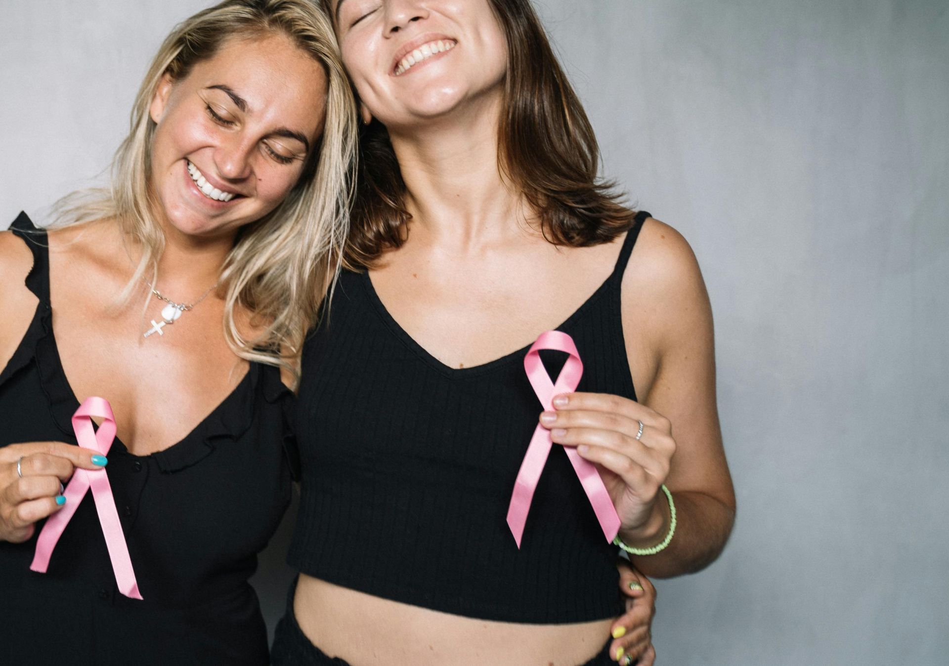 Two smiling women holding pink ribbons, symbolizing breast cancer awareness and support.