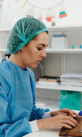 A female healthcare professional in scrub suit working on a computer in a laboratory setting.