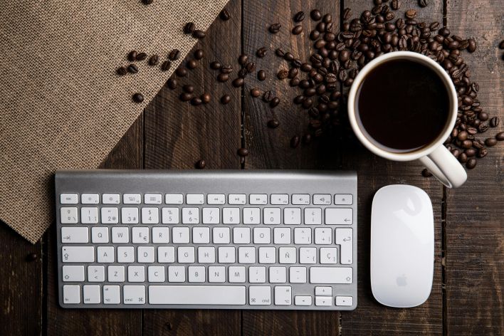 Top view of a coffee cup with keyboard and mouse on a rustic wooden desk.